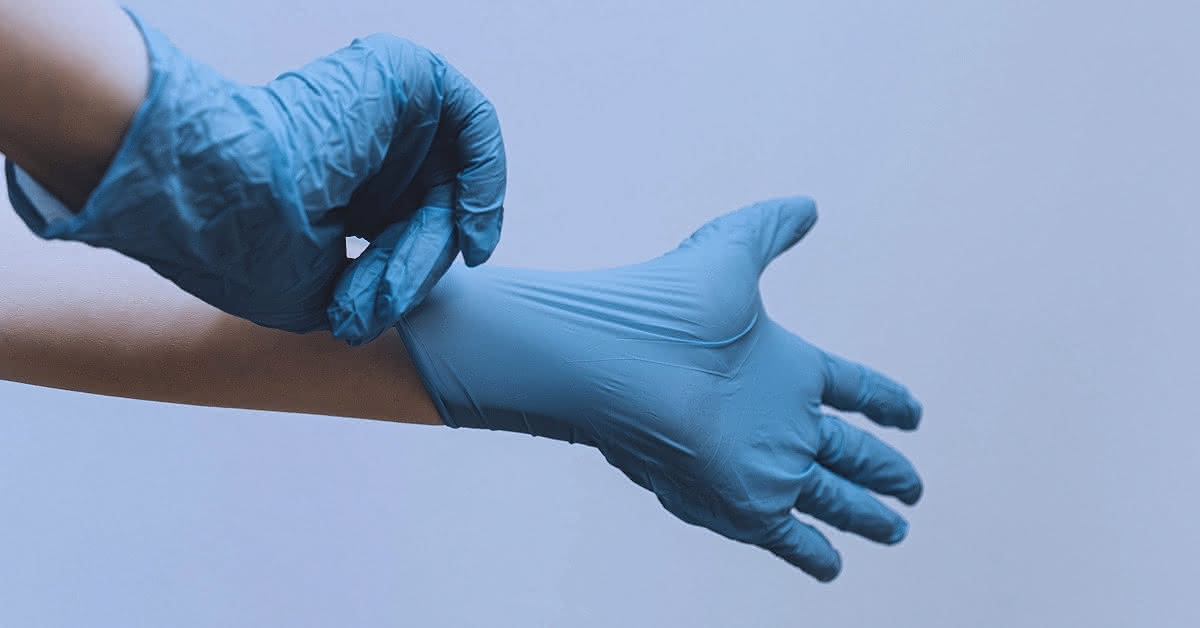Hands putting on blue vinyl gloves, before a blank background