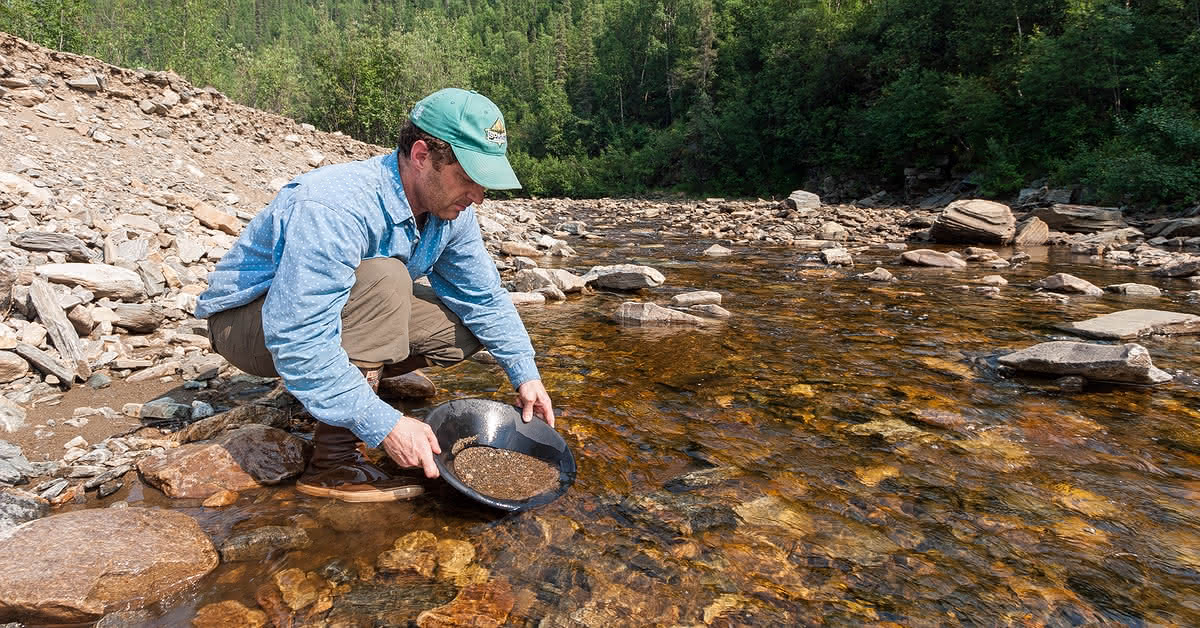 A crouching man pans for gold at a public gold panning area on Jack Wade Creek, in Alaska.